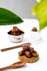 Portrait image of delicious sweet dates, sweet dried dates fruit popular during Ramadan, typical fruit of fasting month. served on white table with ornamental plants, wooden spoon and fork