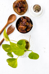 Portrait image of delicious sweet dates, sweet dried dates fruit popular during Ramadan, typical fruit of fasting month. served on white table with ornamental plants, wooden spoon and fork