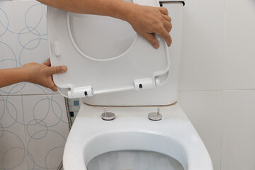 Handyman replace toilet seat cover.  Bathroom toilet seat replacement concept.