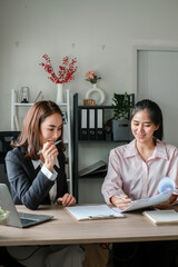 Two women engaged in a business discussion at a modern office desk with documents and a laptop.