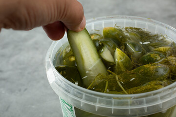 A closeup view of a hand pulling out a pickle from a plastic container.