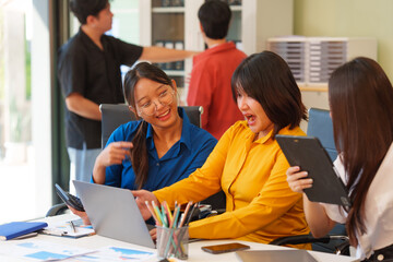 A young Asian startup business team collaborating on a project in a modern office, using a laptop, analyzing graphs, planning business strategies,leveraging online technology for innovation growth