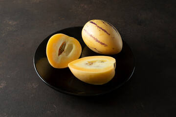 A view of some pepino melons on a plate, featuring one melon that is halved.