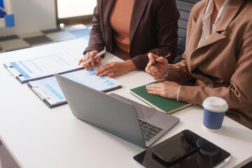 Close-up of two businesswomen working at desk discussing business strategies, analyzing financial charts, planning marketing plans and using laptop to drive business growth in professional office