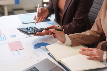 Close-up of two businesswomen working at desk discussing business strategies, analyzing financial charts, planning marketing plans and using laptop to drive business growth in professional office