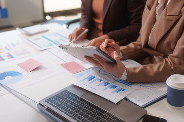 Close-up of two businesswomen working at desk discussing business strategies, analyzing financial charts, planning marketing plans and using laptop to drive business growth in professional office