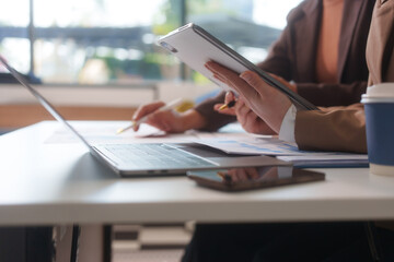 Close-up of two businesswomen working at desk discussing business strategies, analyzing financial charts, planning marketing plans and using laptop to drive business growth in professional office