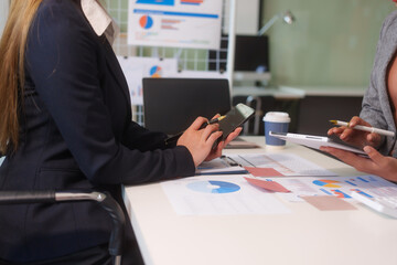 Close-up of two businesswomen working at desk discussing business strategies, analyzing financial charts, planning marketing plans and using laptop to drive business growth in professional office
