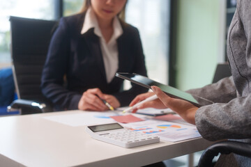 Close-up of two businesswomen working at desk discussing business strategies, analyzing financial charts, planning marketing plans and using laptop to drive business growth in professional office