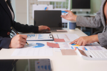Close-up of two businesswomen working at desk discussing business strategies, analyzing financial charts, planning marketing plans and using laptop to drive business growth in professional office