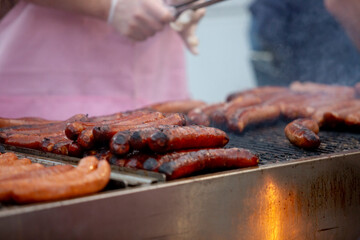 A view of a pit master cooking sausages on a grill, seen at a local food festival.
