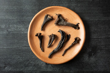 A top down view of several black trumpet mushrooms, on a clay plate.
