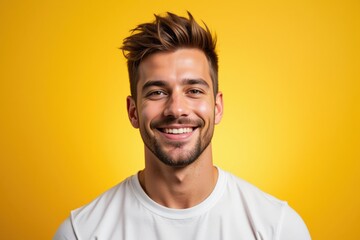 Obraz premium Young Caucasian Male with Short Brown Hair Smiling against a Bright Yellow Background, Exuding Positivity and Confidence in a Casual White T-shirt