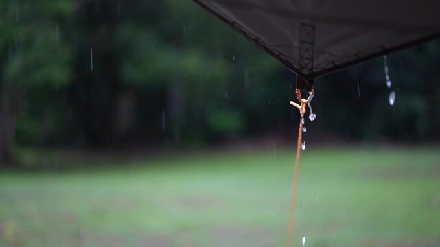 rainy season camping with heavy rain water drips droplets to tip tarp and flow slow motion on fly sheet tent with carabiner paracord rope umbrella by holiday travel picnic on nature forest garden