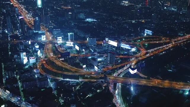 Illuminated multi-level highway stack interchange in center of Bangkok city at night. Many cars move through traffic jam