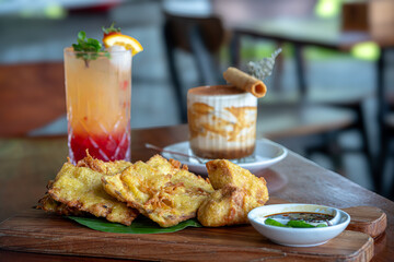A tiramisu dessert, likely served in a glass together with tropical punch drinks and a portion of fried tempeh, tofu and bakwan on the table