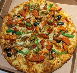 A delicious pizza with a golden-brown crust, mozzarella cheese, spicy tandoori chicken, sliced pepperoni, and red chili peppers. The pizza is placed in an open cardboard box, ready to be served.