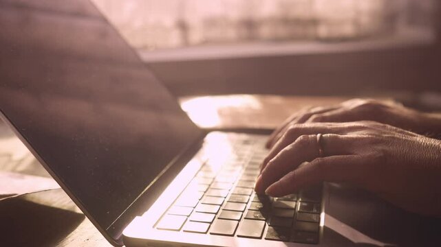 Close-up of hands typing on laptop in soft warm morning sunlight.