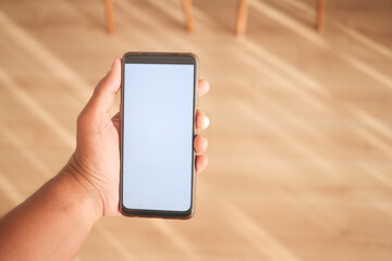 Hand holding a blank smartphone indoors with wooden flooring