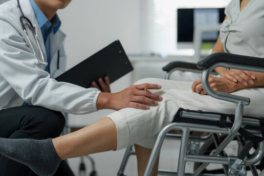 Doctor examining senior woman's knee in wheelchair at hospital - Powered by Adobe