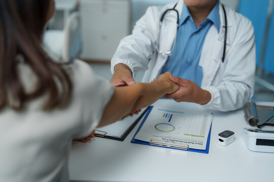 Doctor comforting patient by holding her hand at clinic