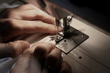 The hands of a person working on a sewing machine. The machine＇s needle passes through the fabric, which the person guides with his hands. 