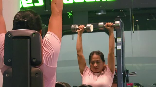 Beautiful Asian woman doing exercise in the gym with dumbbell and facing the mirror.