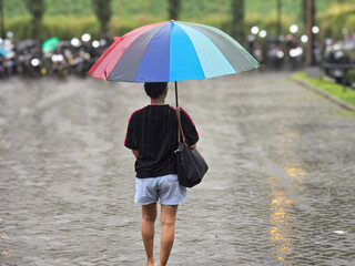 back view of woman using colorful umbrella walking in heavy rain outdoors