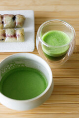 Cup of fresh matcha tea, green tea and Coconut steamed sticky rice with banana, Thailand dessert on wooden table.