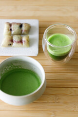 Cup of fresh matcha tea, green tea and Coconut steamed sticky rice with banana, Thailand dessert on wooden table.