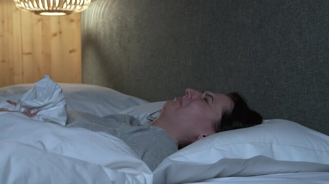 Morning routine of brunette woman softly leaving rumpled bed, gently moving sheets and pillows while emerging from cozy bedroom space