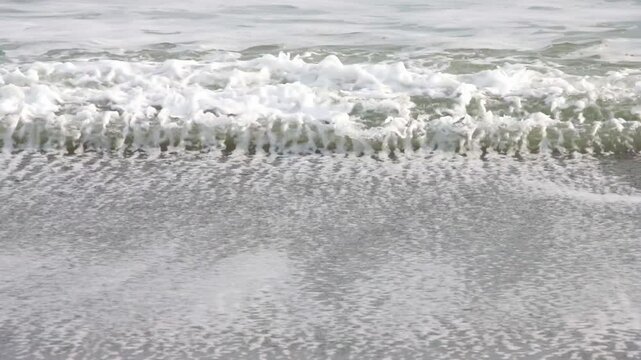 Three parallel frothy sea water waves breaking on sandy beach