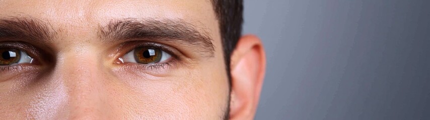 Obraz premium Close up of a man's face, focusing on his brown eyes and slightly damp skin. Neutral gray background