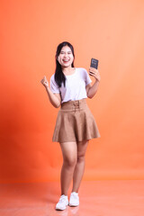 A cheerful Asian woman celebrates good news on her smartphone with a joyful expression and positive...