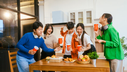 Five young Asian men and women gather around a kitchen desk, enjoying a party with drinks, fried chicken, and bread. They share laughter, good food, and happiness in a lively atmosphere.