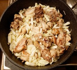 A pan of chicken and onions is cooking on a stove