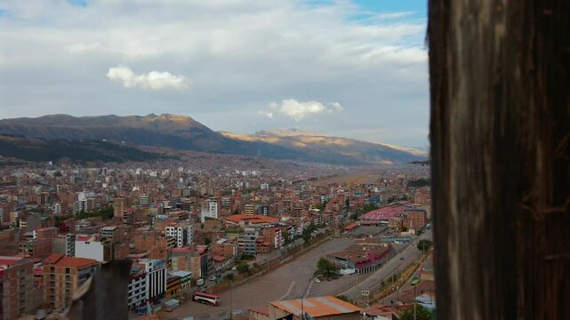 A breathtaking view from Mirador Pachacutec in Cusco, Peru, showcasing the cityscape, streets, and mountains under a partly cloudy sky.