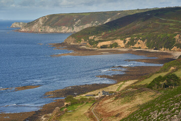 Scenic view of Normandy’s coastline in France, featuring a blue sea, rugged cliffs, green hills, and a small settlement.