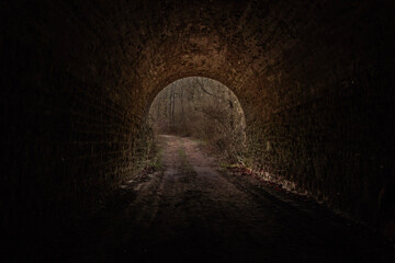 Obraz premium A dark, atmospheric view of a tunnel leading into a brighter, more open space. At the end of the tunnel, an area of ​​brighter light is visible, suggesting an exit or opening into a more open area.