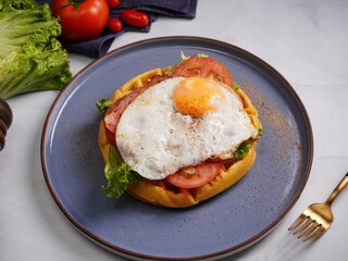 Fresh waffles with fried eggs, lettuce, tomatoes and served for breakfast on a flat table.