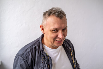 Fototapeta premium Portrait of a cheerful middle-aged smiling man wearing a gray hoodie, standing against a textured stone wall in natural light.