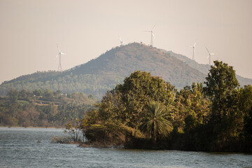 Wind turbines on a mountain overlooking a serene lake with lush greenery on a clear day