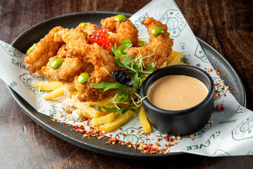 Crispy fried shrimp served on a bed of golden French fries, garnished with vibrant herbs and a side of creamy dipping sauce, perfect for seafood lovers.