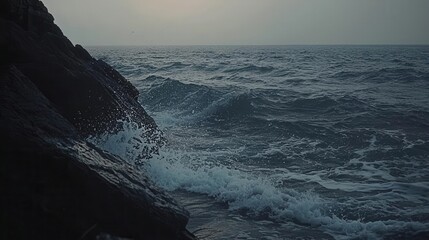 Ocean waves crashing against dark rocks at sunset