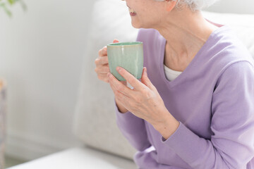 ソファーでコーヒーを飲みながらくつろぐシニア女性	
