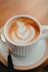 Delicious Latte Art in a White Mug on a Saucer with a Spoon on a Wooden Table, Warm Coffee Drink Experience