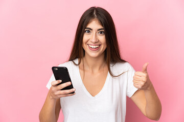 Fototapeta premium Young caucasian woman isolated on pink background using mobile phone while doing thumbs up