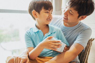 Fototapeta premium Asian boy give a gift box to his father, Dad and son embrass each other with love and happiness, Relationship in family concept. Celebrate for father day and birthday in living room.