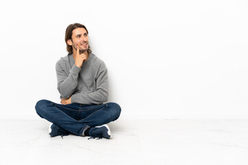 Young handsome man sitting on the floor over isolated background thinking an idea while looking up