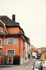 A European street lined with historic buildings featuring red-tiled roofs and vibrant facades. The quaint atmosphere captures the essence of traditional European architecture.